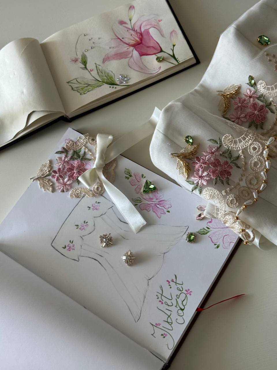 Hand-painted sketchbook beside embroidered lace
